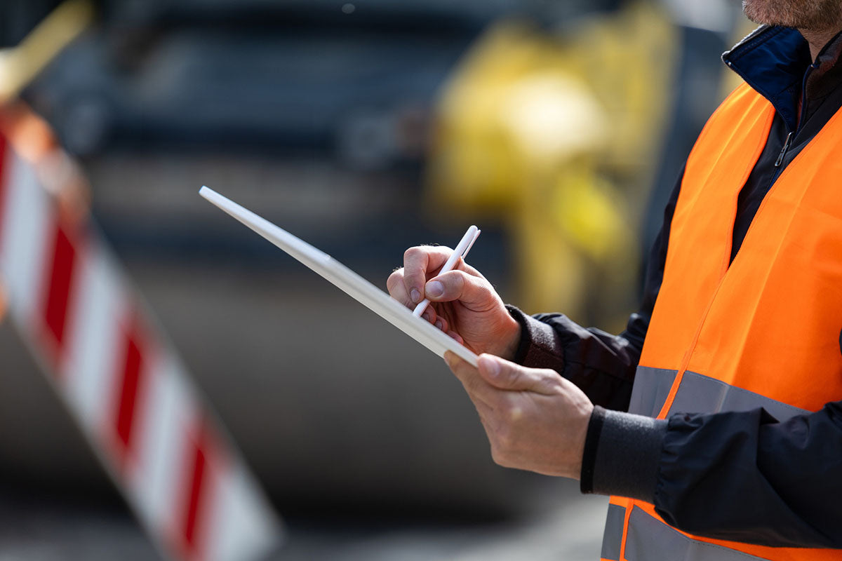 Close-up of a worker in a safety vest using a tablet to conduct an electrical site inspection.